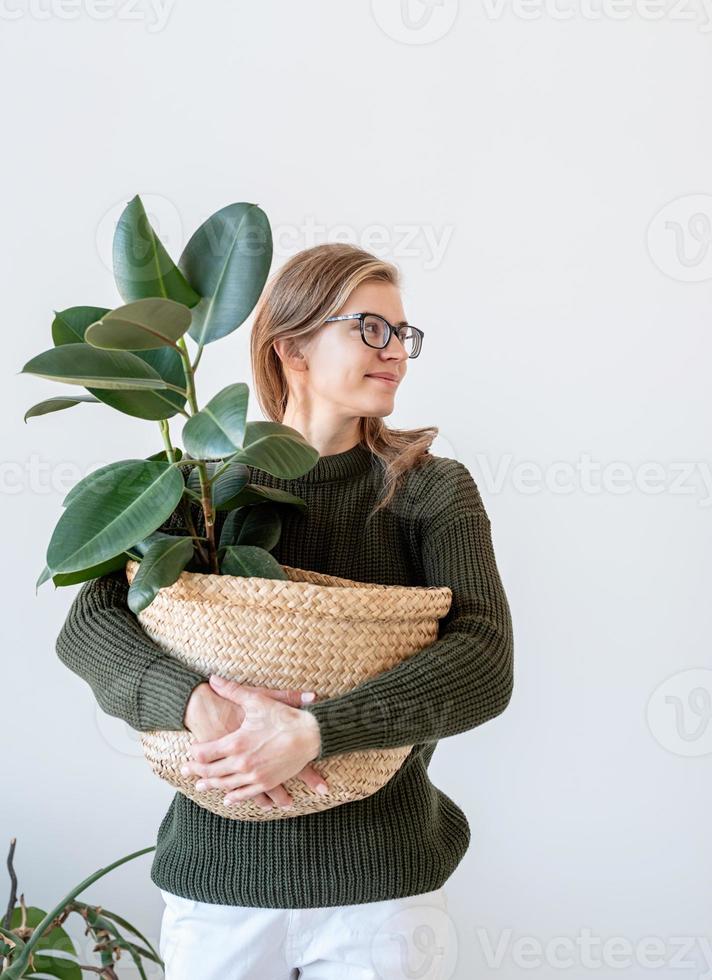 attraente giovane donna in interni luminosi e ariosi con in mano una pianta di ficus foto