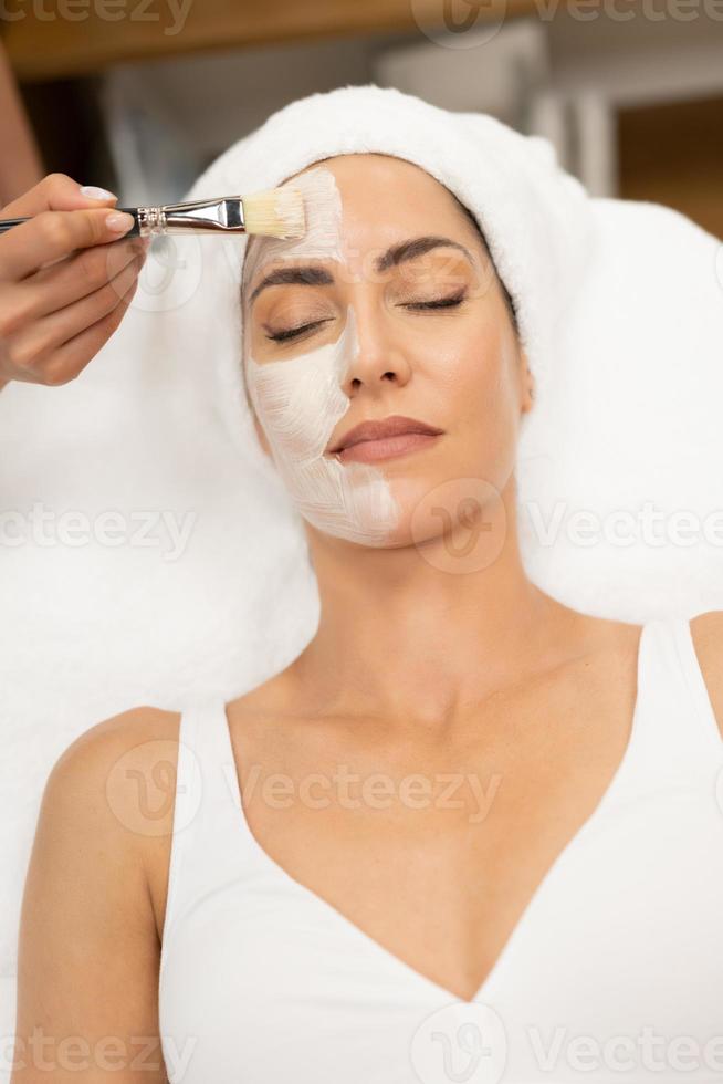 estetica applicando una maschera al viso di una donna di mezza età nel moderno centro benessere. foto