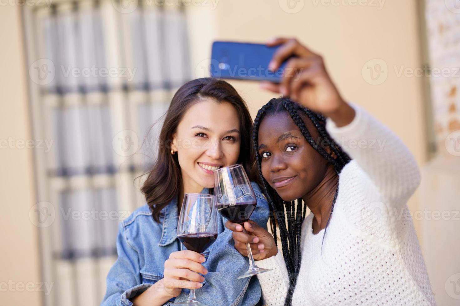 due donne che si fanno un selfie con uno smartphone mentre bevono un bicchiere di vino. foto