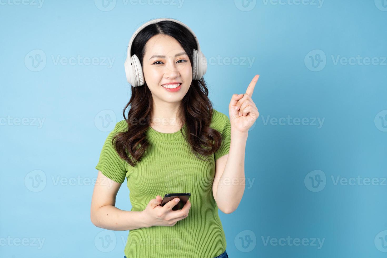 il ritratto asiatico della ragazza della cavalletta sta ascoltando la musica, isolato su fondo blu foto