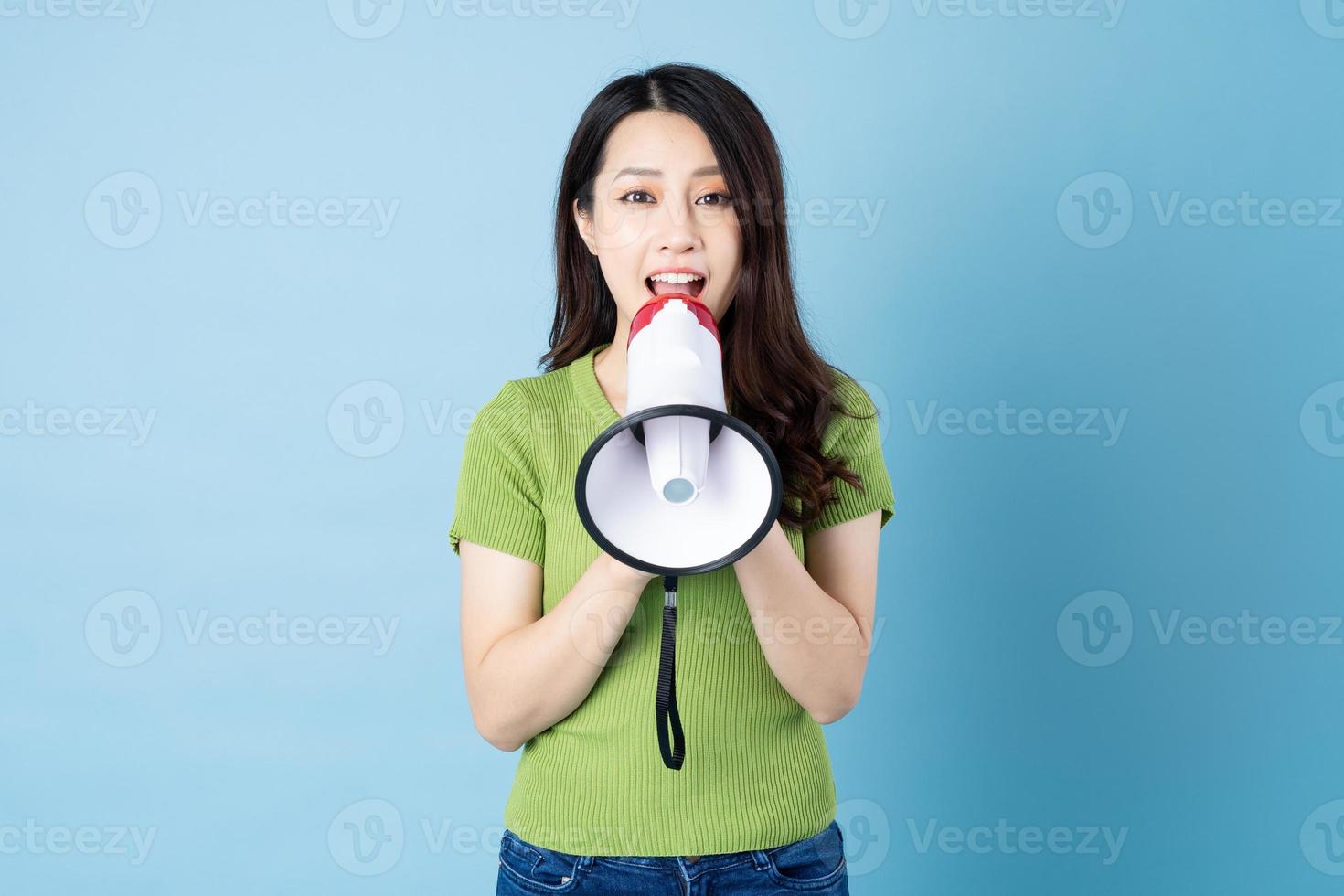 Ritratto di ragazza asiatica che tiene altoparlante, isolato su sfondo blu foto