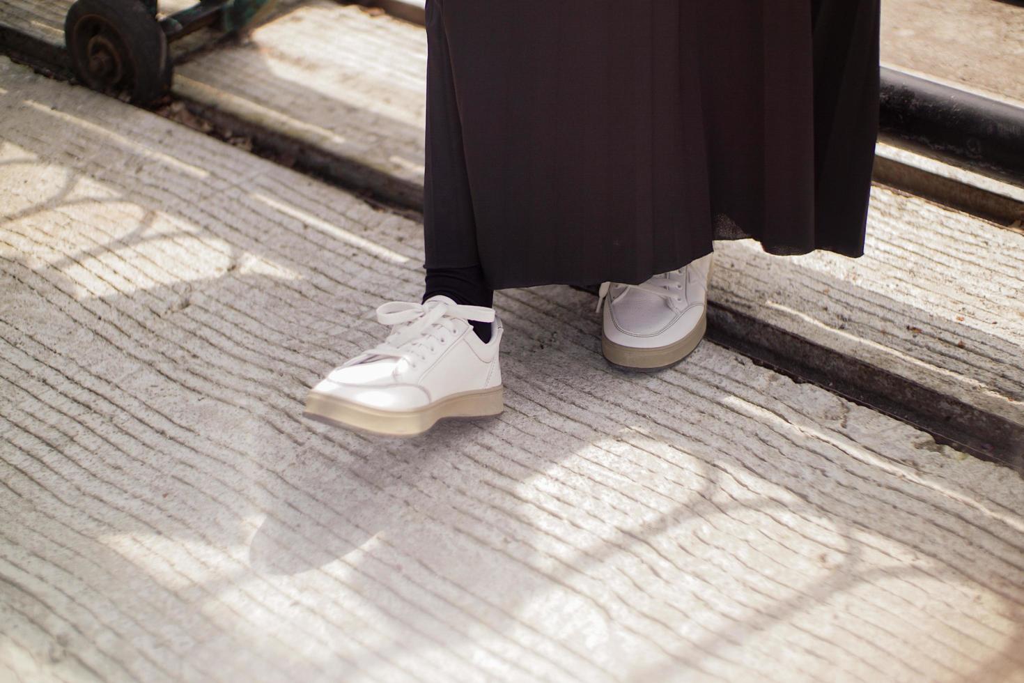 i piedi di una donna che indossa una gonna nera e scarpe bianche. potrebbe fare un passo per spostarsi dalla sua posizione. foto