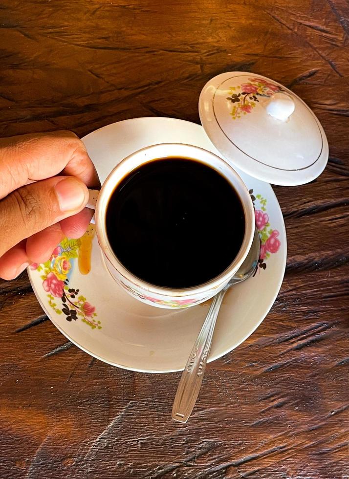 una tazza di caffè caldo è sul tavolo. una ragazza tiene in mano una bevanda gustosa. foto