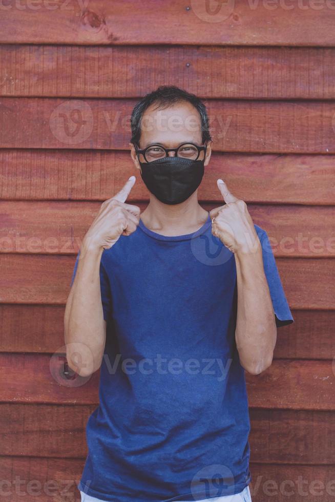 uomo asiatico che indossa una maschera di protezione per il viso in piedi contro la parete di legno foto