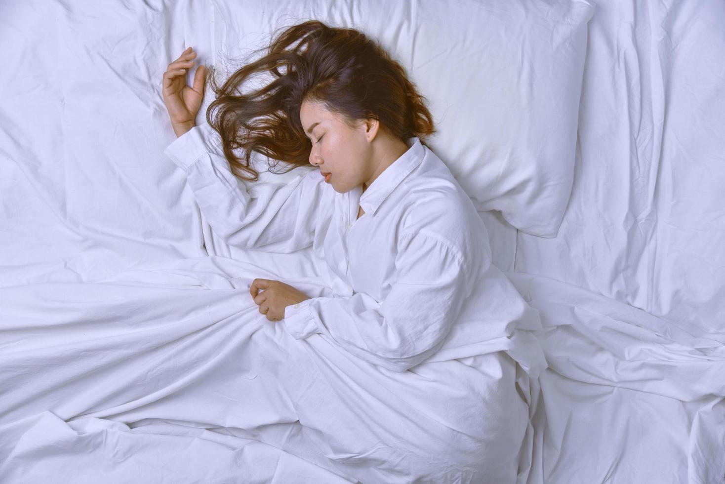 giovane donna che dorme nel letto. vista dall'alto della giovane donna sdraiata che dorme bene a letto. dormire rilassati, la giovane bella signora sorridente giace a letto. foto