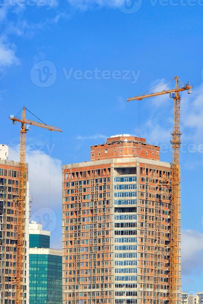 le gru a torre sono ancorate a moderni edifici residenziali in costruzione su uno sfondo di cielo blu. foto