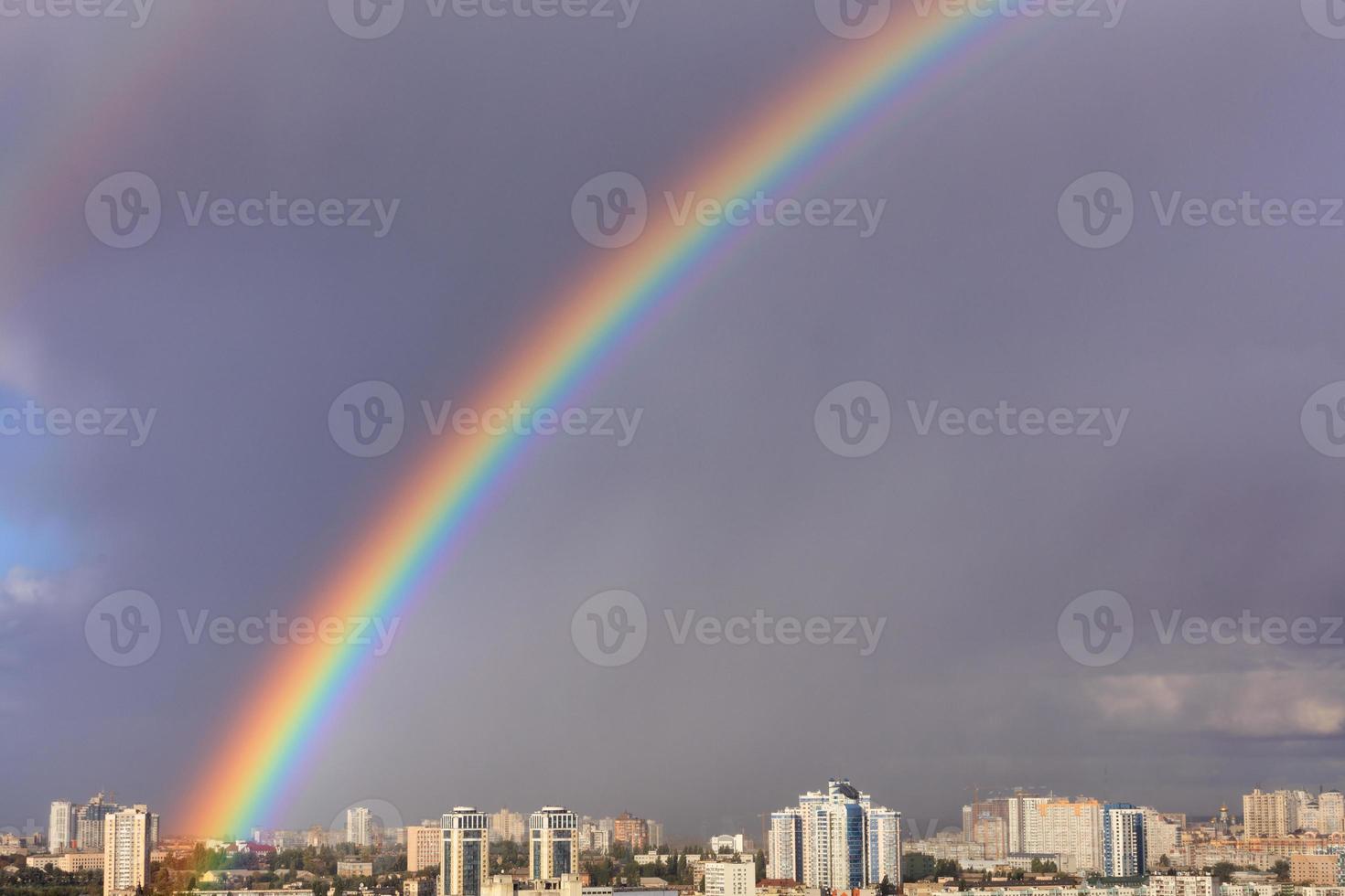 un grande arcobaleno luminoso nel cielo grigio sopra la città dopo l'ultimo temporale. foto