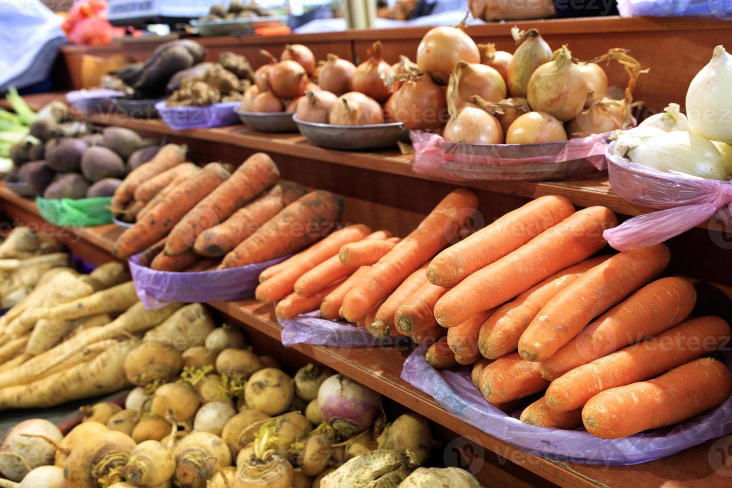 carote, cipolle, radici e altre verdure varie sono vendute sugli scaffali del mercato foto