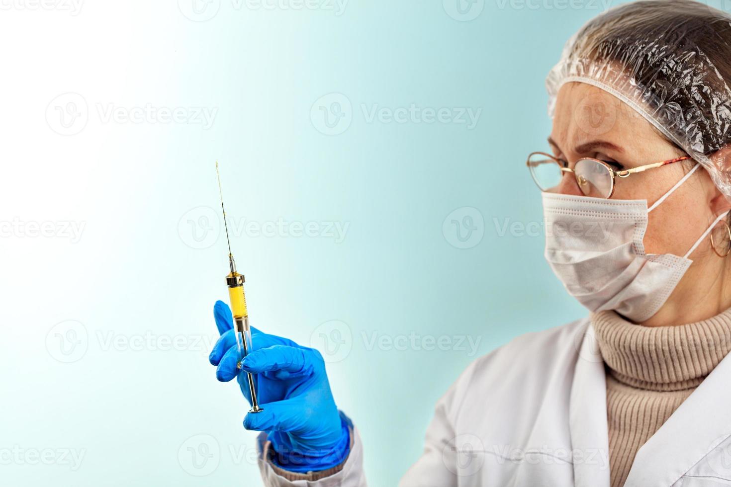un medico con un guanto medico in lattice controlla il vaccino da una piccola siringa. il concetto di protezione contro i virus. tema medico su uno sfondo turchese chiaro. foto