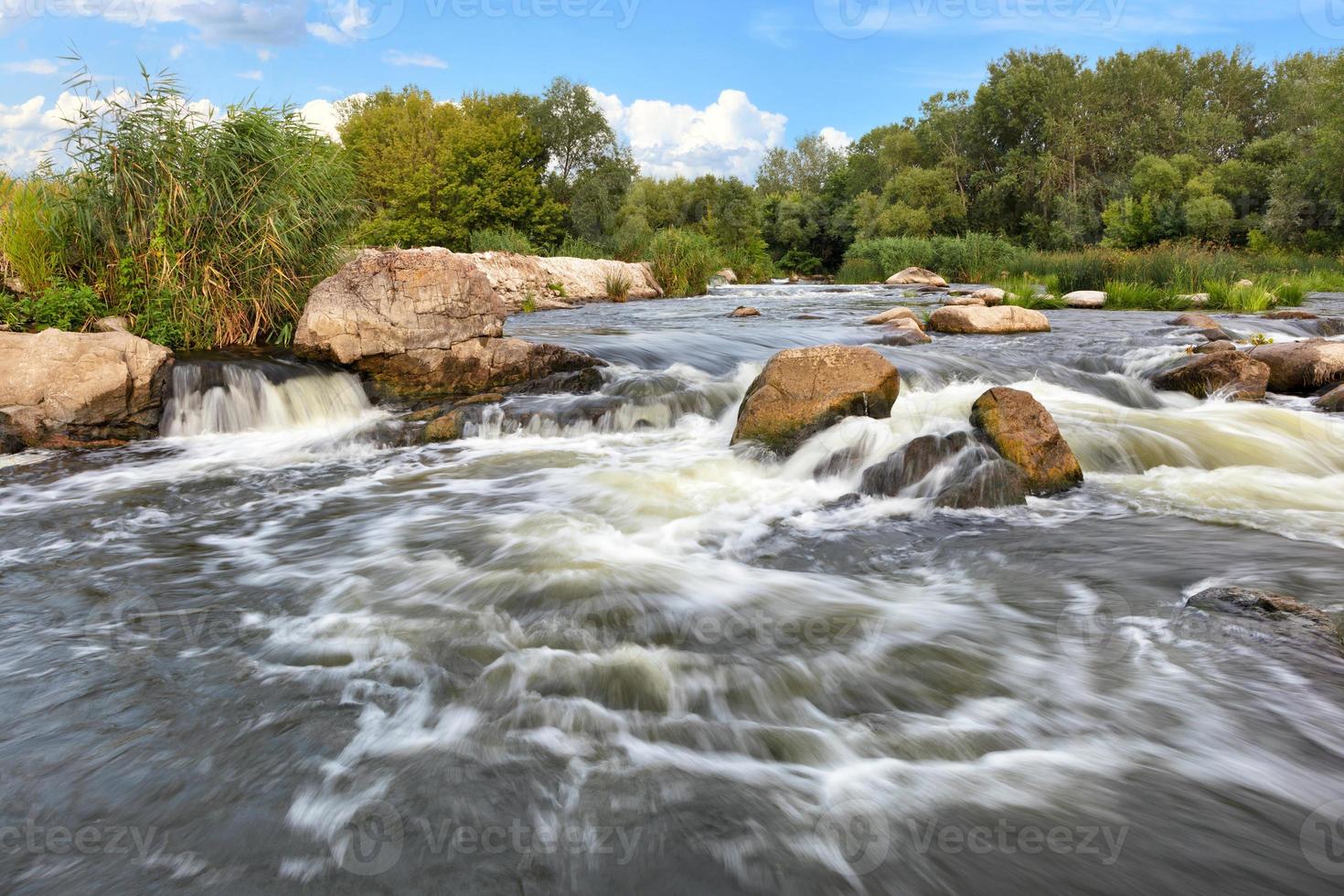 tempestosi corsi d'acqua si lavano sulle sponde rocciose del fiume, superando le rapide in una luminosa giornata estiva. foto