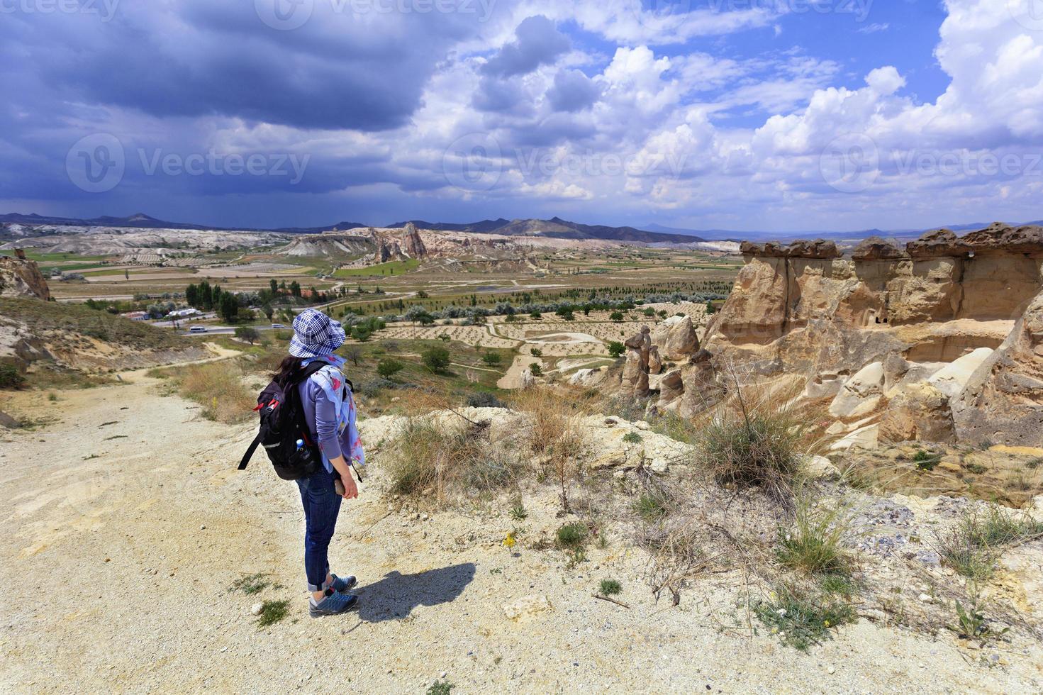 una giovane ragazza si trova sul bordo di una scogliera in cappadocia e ammira lo spazio circostante sullo sfondo di un cielo nuvoloso tempestoso e un paesaggio montano. foto