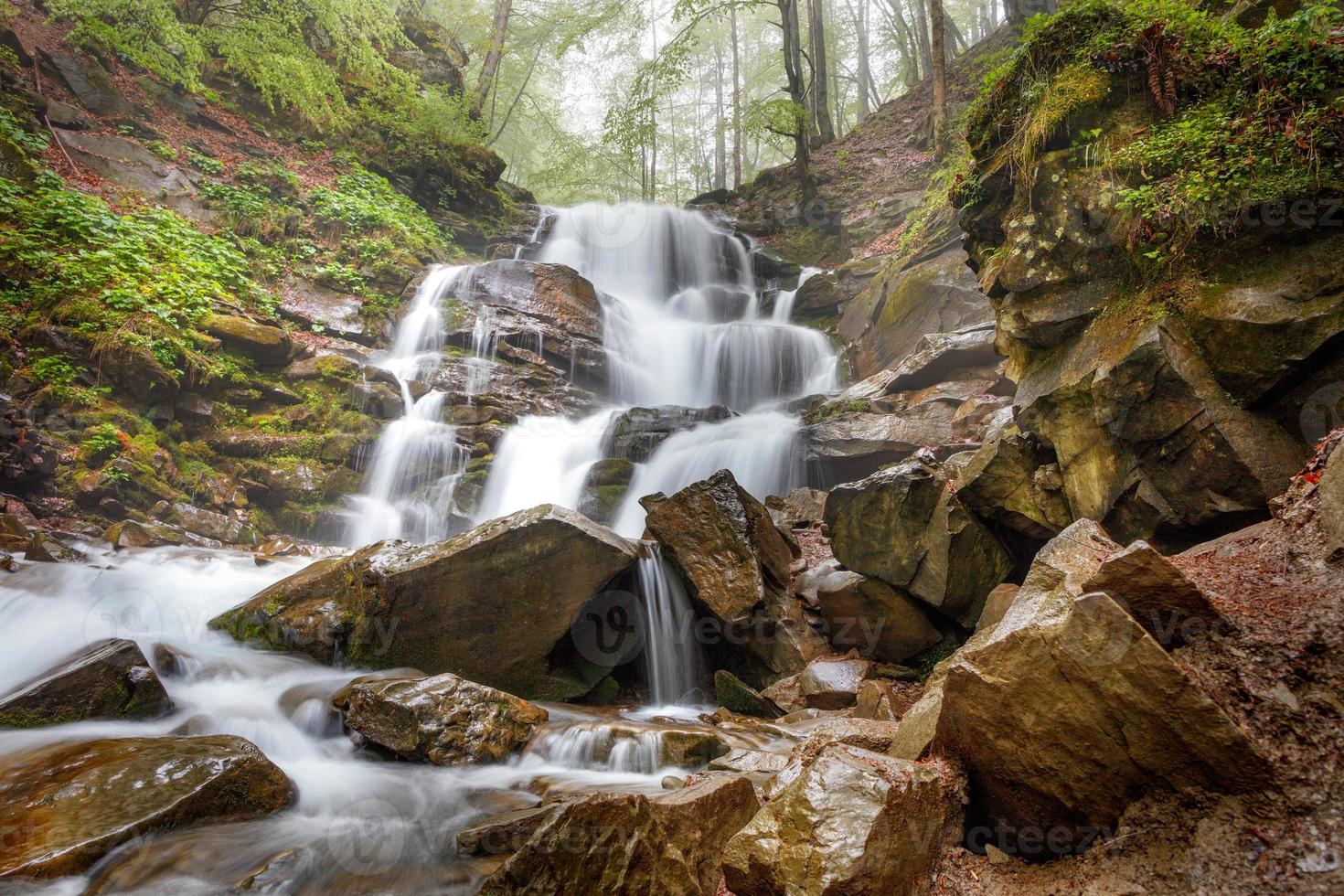 il rapido flusso delle cascate d'acqua del fiume di montagna e dei fili biancastri si fa strada attraverso il terreno collinare della foresta rocciosa in primavera. foto