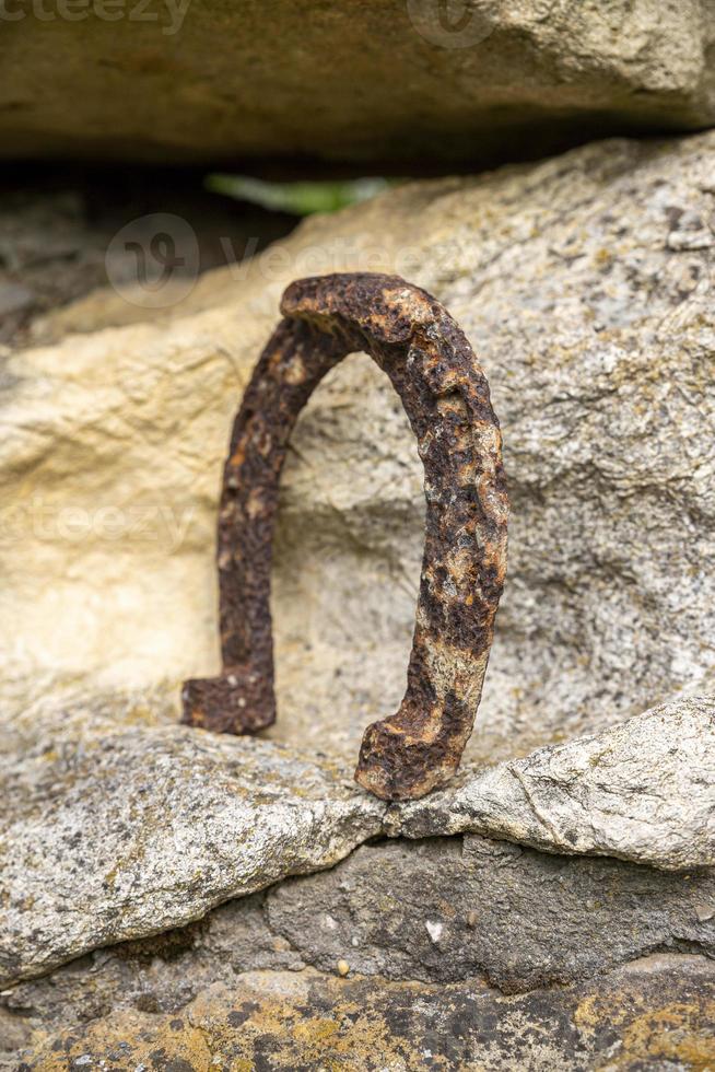 primo piano di un vecchio ferro di cavallo arrugginito appoggiato su una grossa pietra. foto