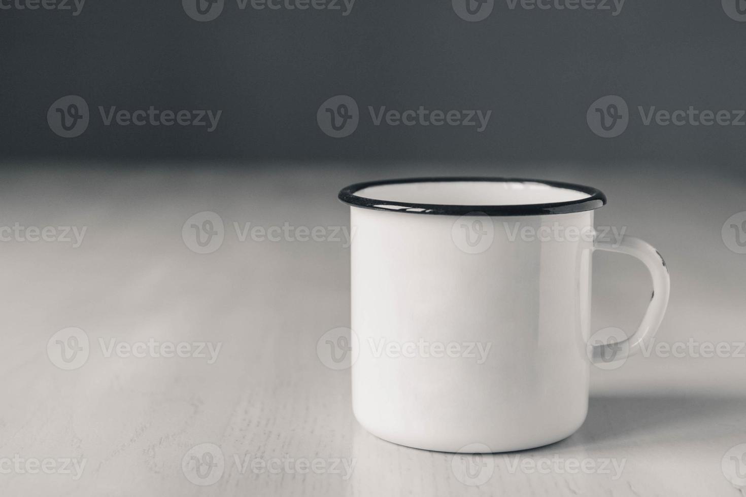 tazza in metallo smaltato bianco con linea nera sul bordo su tavolo in legno bianco foto