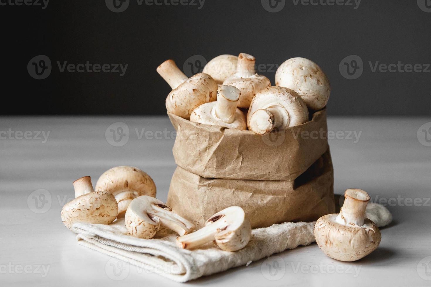 funghi champignon in sacchetto di carta su un tavolo di legno bianco su sfondo scuro foto