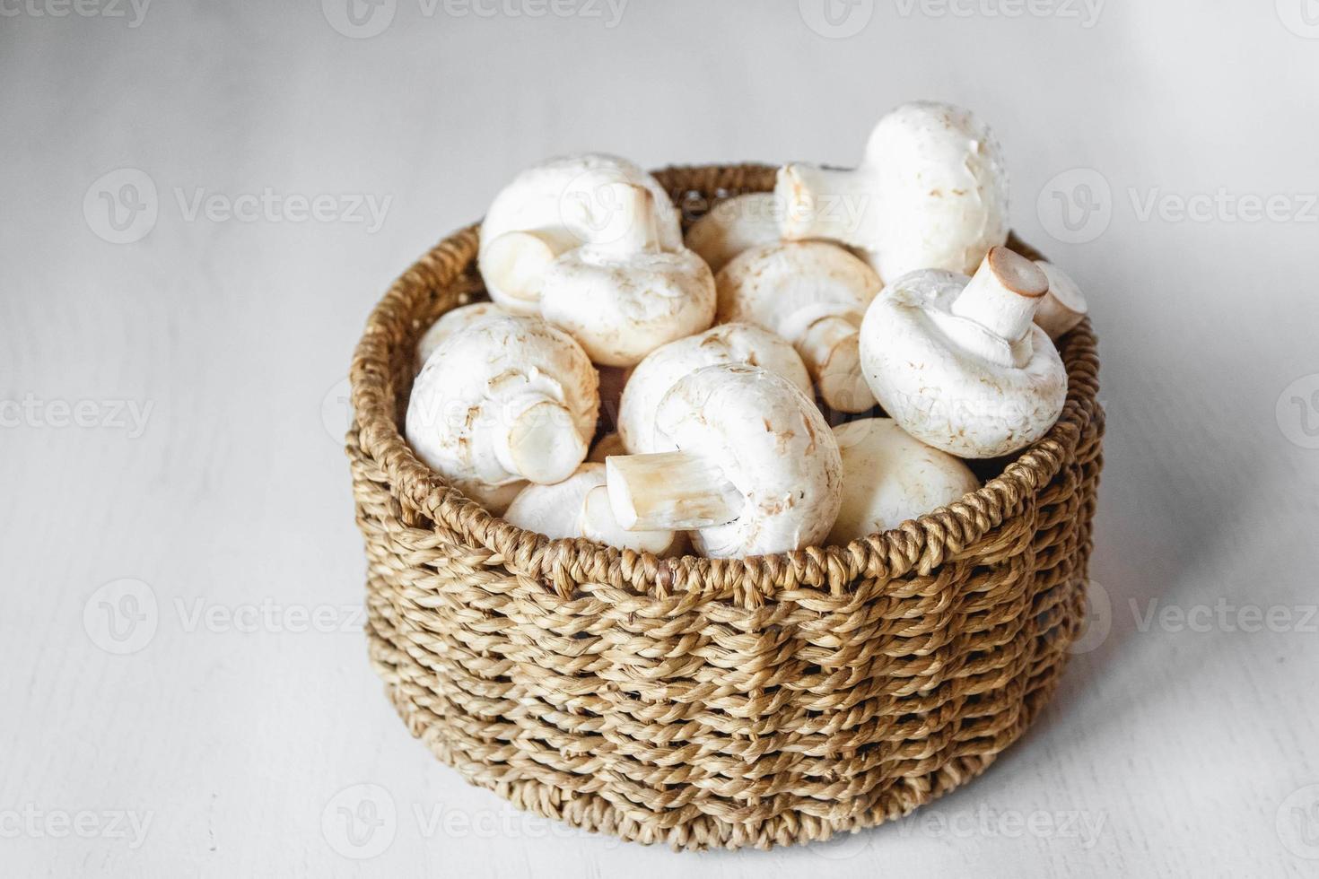 funghi champignon in un cesto di vimini rotondo su un tavolo di legno bianco foto
