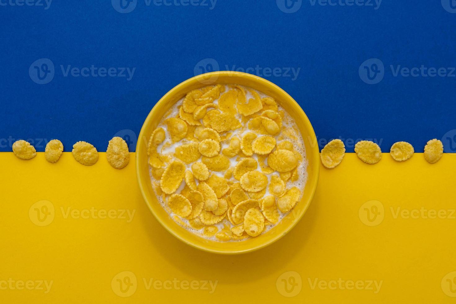 cornflakes con latte nella ciotola gialla su sfondo blu e giallo foto