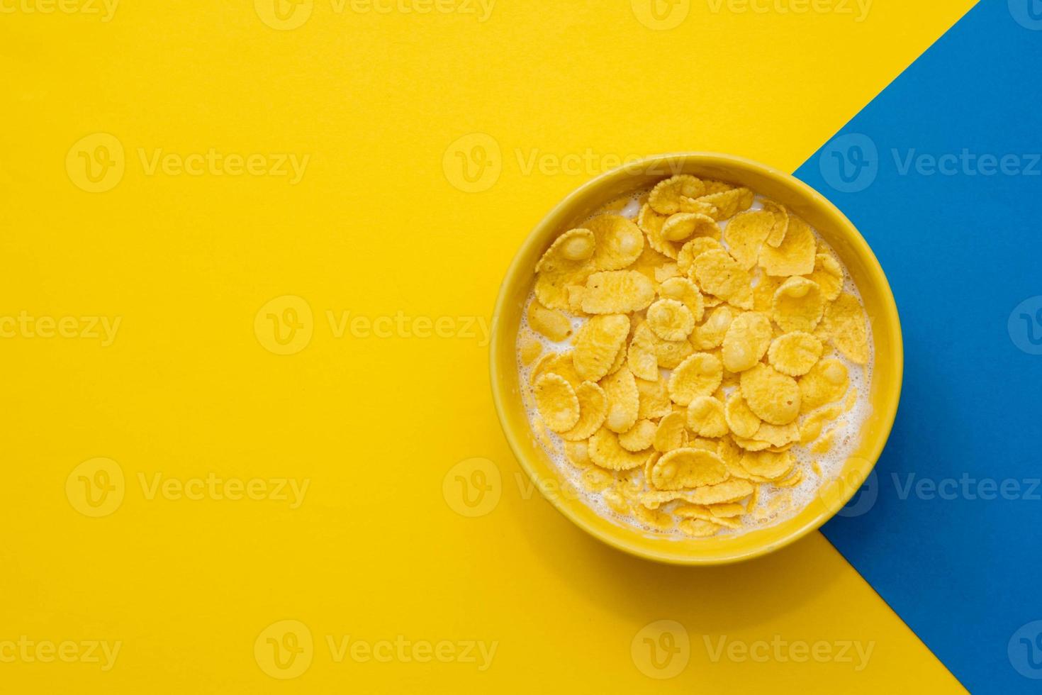 cornflakes con latte nella ciotola gialla su sfondo blu e giallo foto