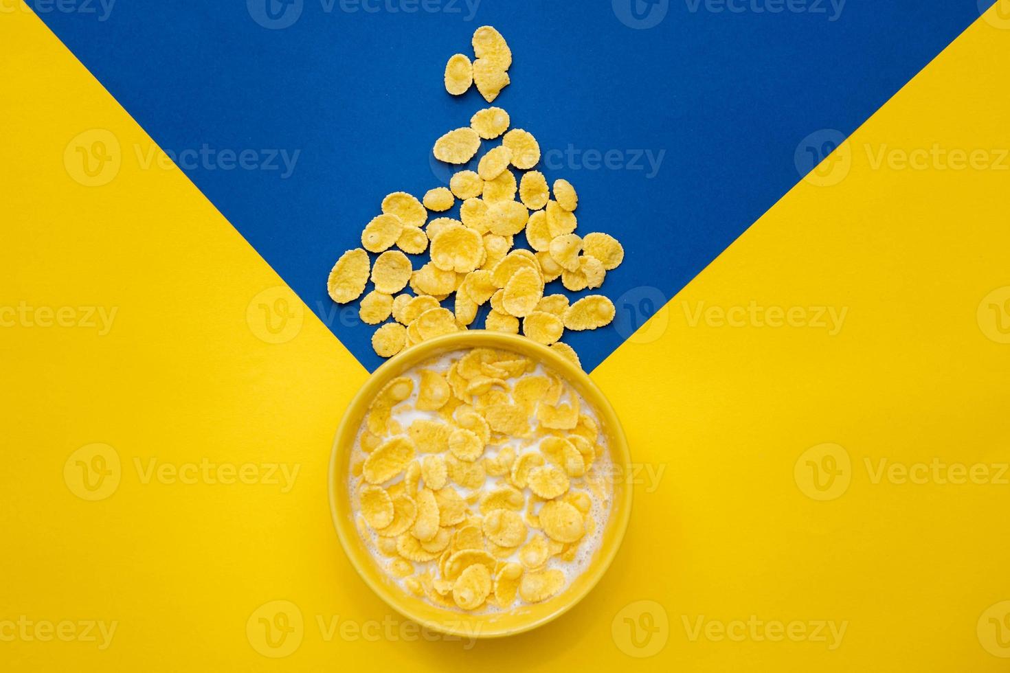 cornflakes con latte nella ciotola gialla su sfondo blu e giallo foto