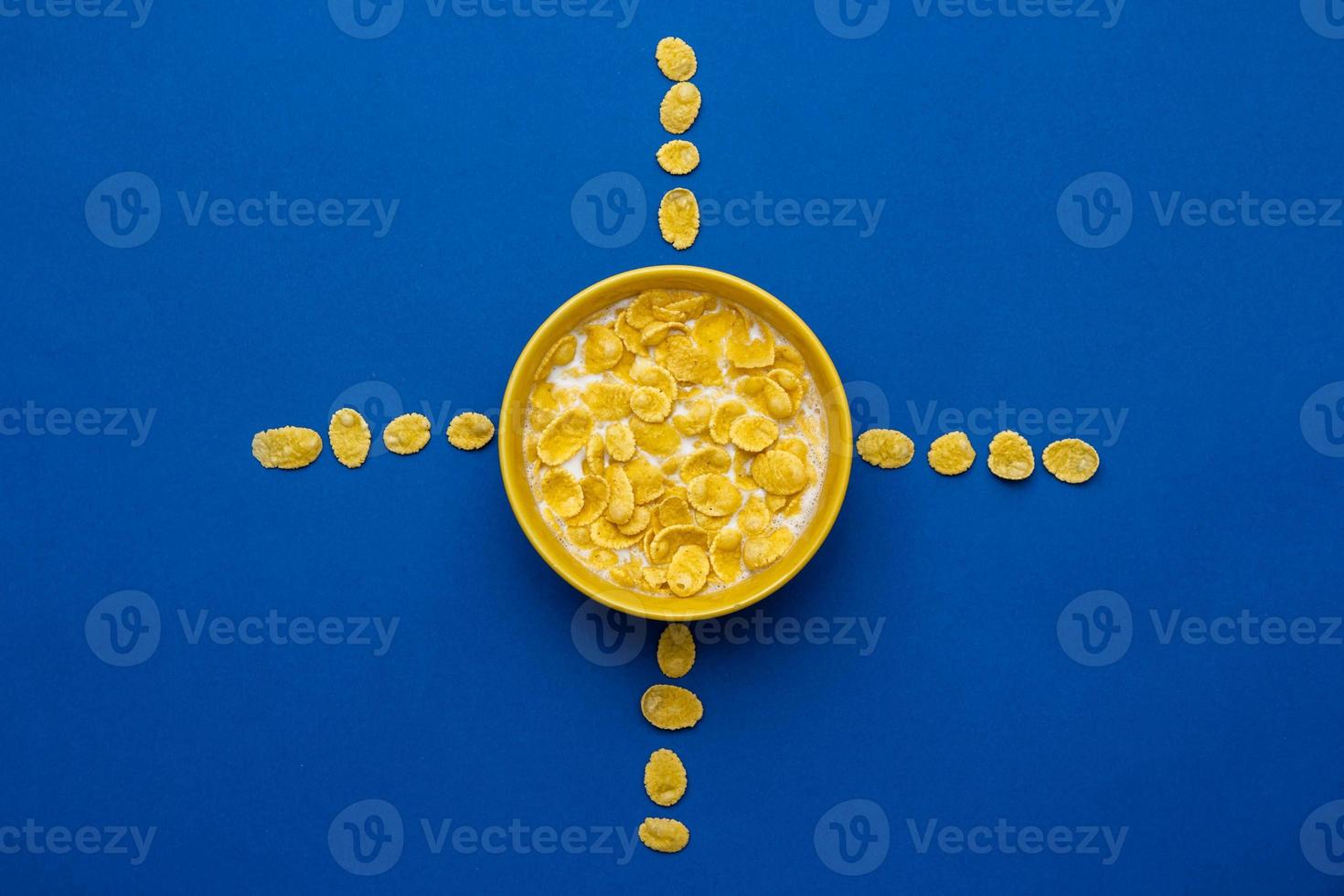 cornflakes con latte nella ciotola gialla a forma di sole su sfondo blu foto