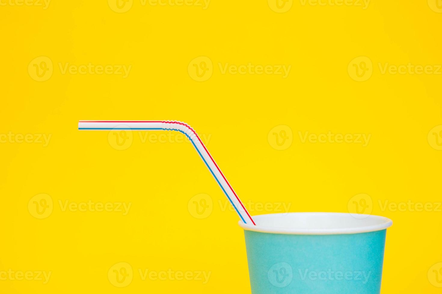 bicchiere di carta blu con cannuccia di plastica colorata su sfondo giallo foto