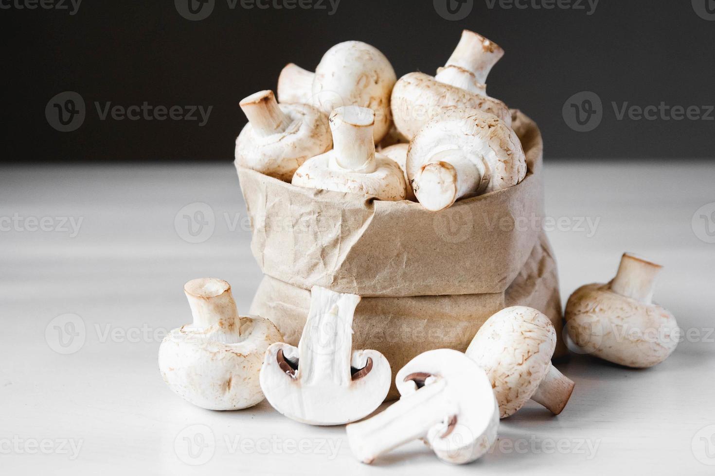 funghi champignon in sacchetto di carta su un tavolo di legno bianco su sfondo scuro foto