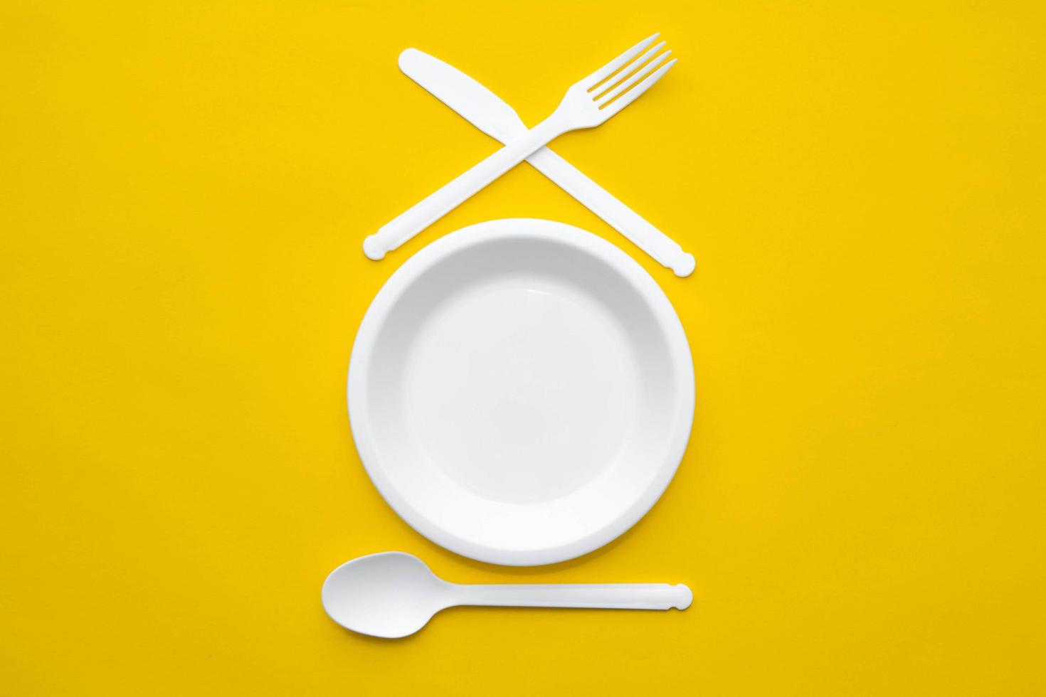 forchetta, coltello, cucchiaio e piatto in plastica bianca su sfondo giallo foto