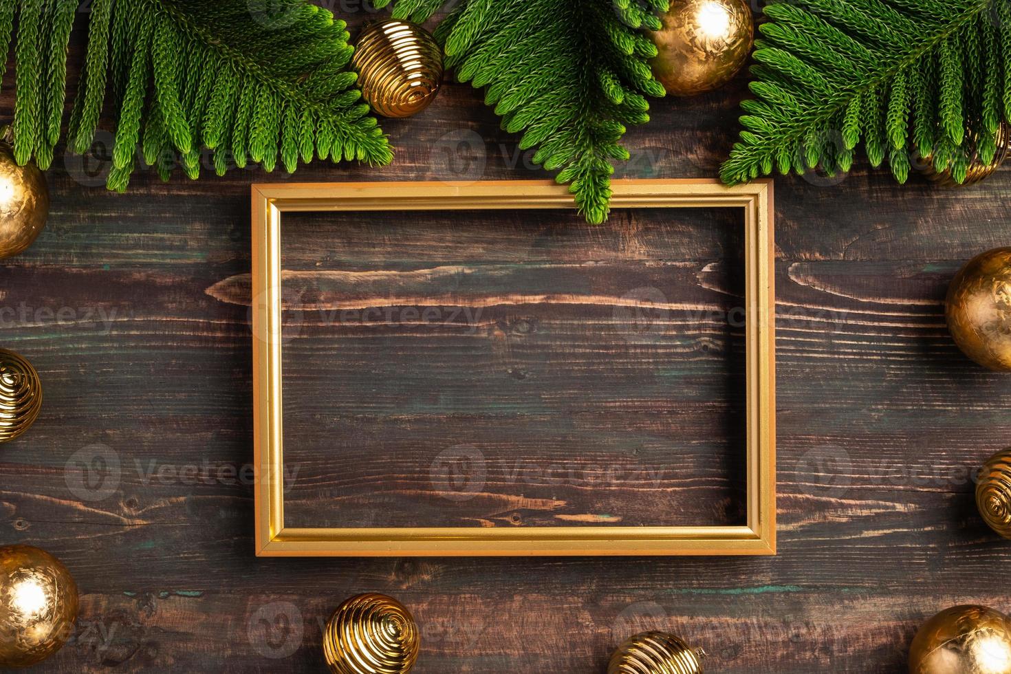 cornice dorata di natale con foglia di pino e decorazioni di palline su tavola di legno foto