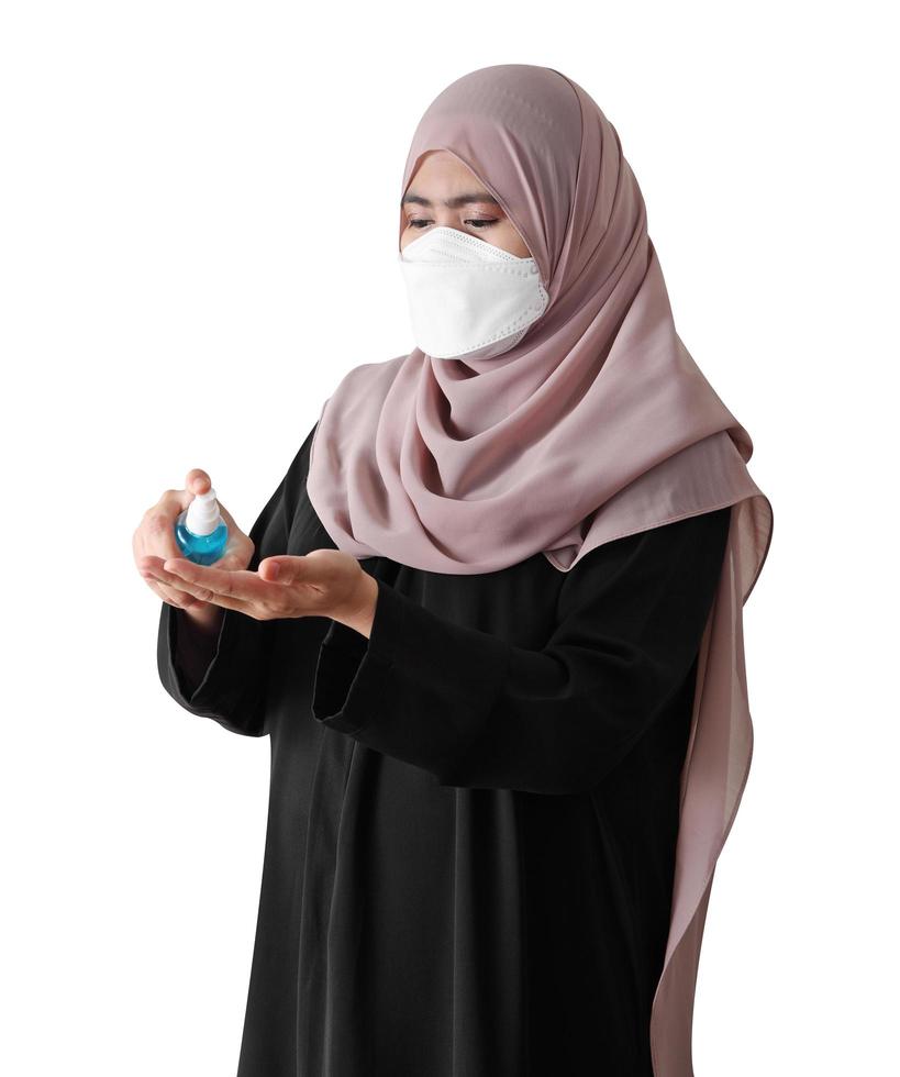 donna musulmana che indossa una maschera chirurgica lavandosi le mani con spray alcolico su sfondo bianco. covid-19 concetto di coronavirus. foto