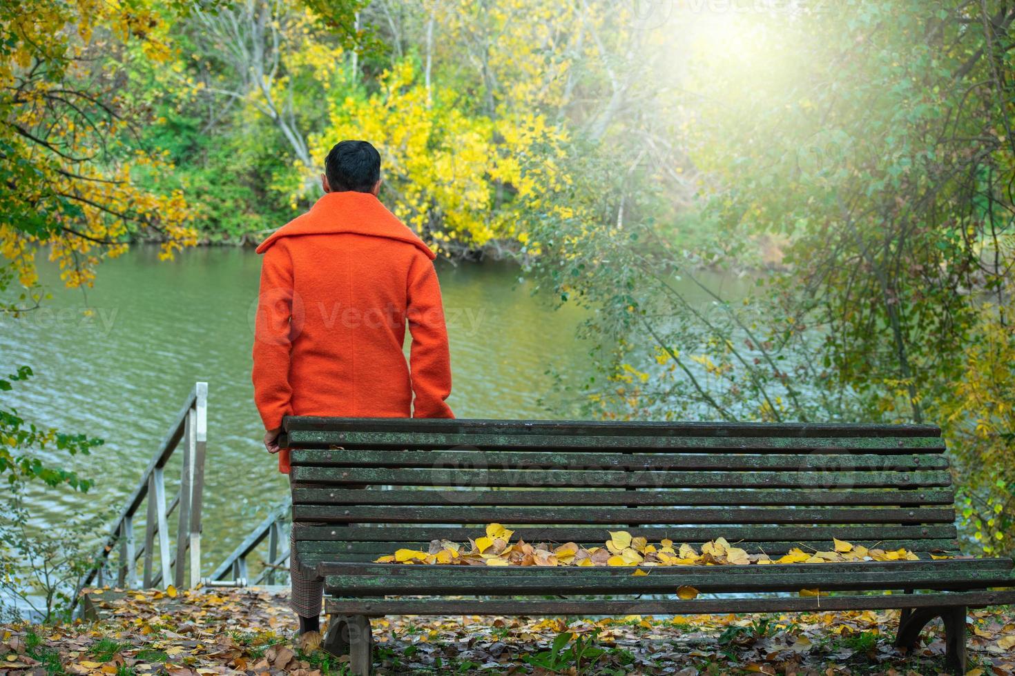 donna sulla schiena in cappotto arancione appoggiata su una panchina nel parco foto