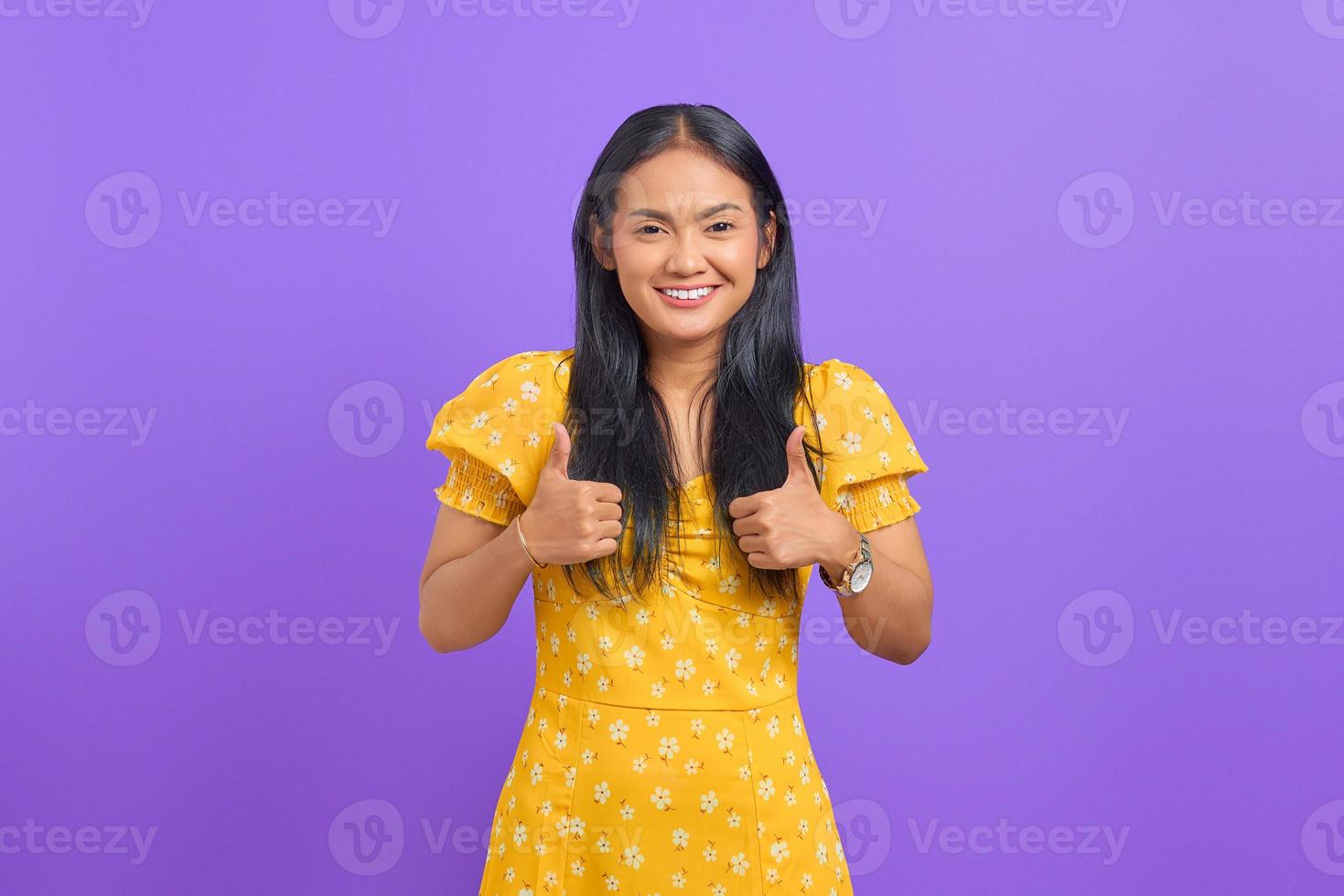 ritratto di giovane donna asiatica sorridente che mostra i pollici in su alla macchina fotografica su sfondo viola foto