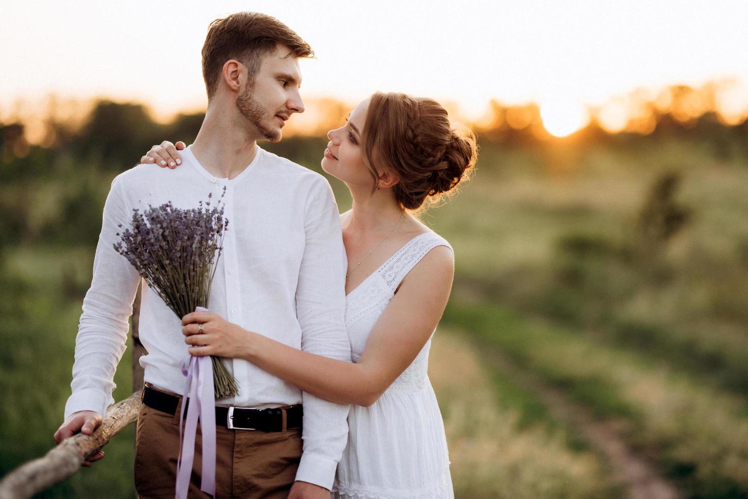 ragazza con un prendisole bianco e un ragazzo con una camicia bianca durante una passeggiata al tramonto con un bouquet foto