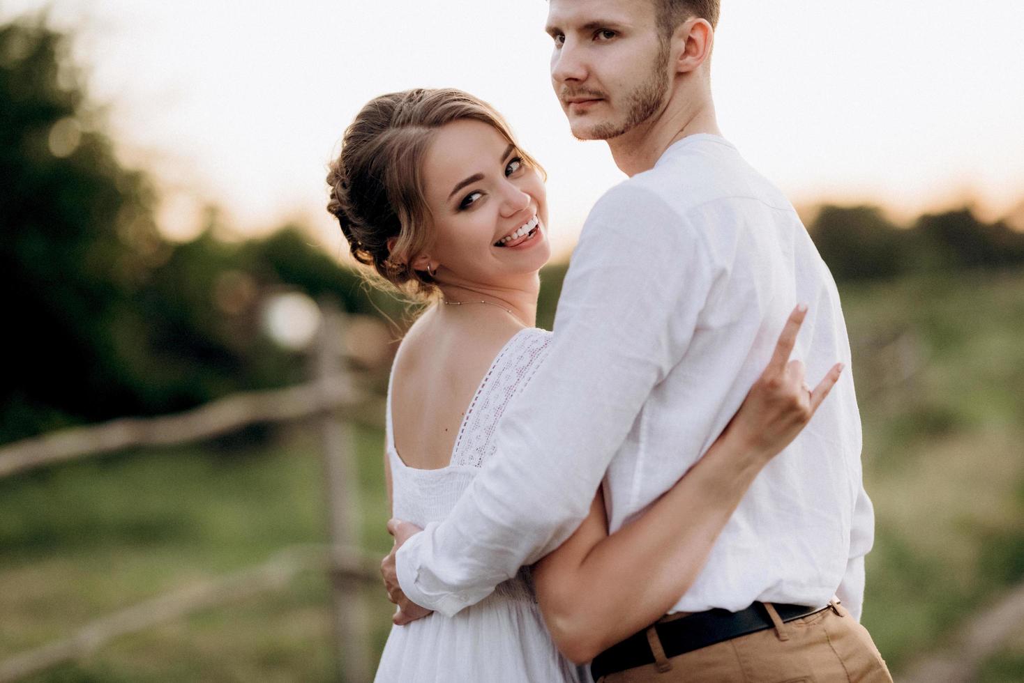 ragazza con un prendisole bianco e un ragazzo con una camicia bianca durante una passeggiata al tramonto con un bouquet foto