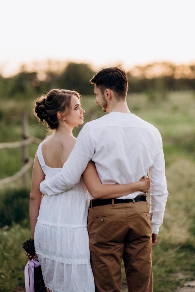 ragazza con un prendisole bianco e un ragazzo con una camicia bianca durante una passeggiata al tramonto con un bouquet foto