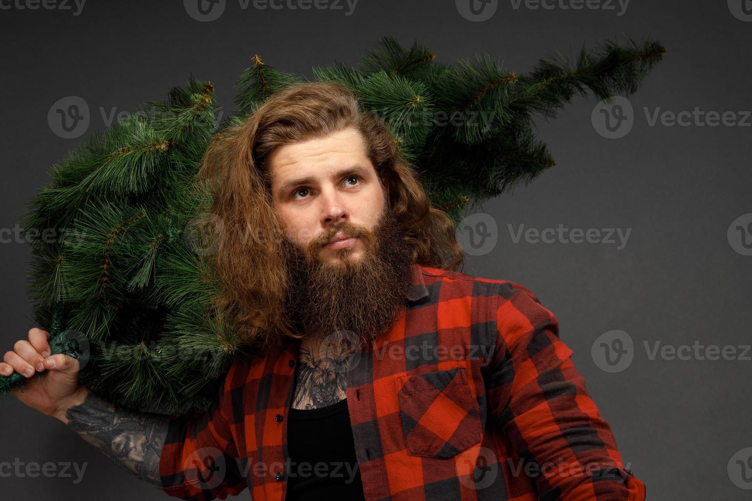 bell'uomo con i capelli lunghi che tiene in mano un albero di natale sintetico foto