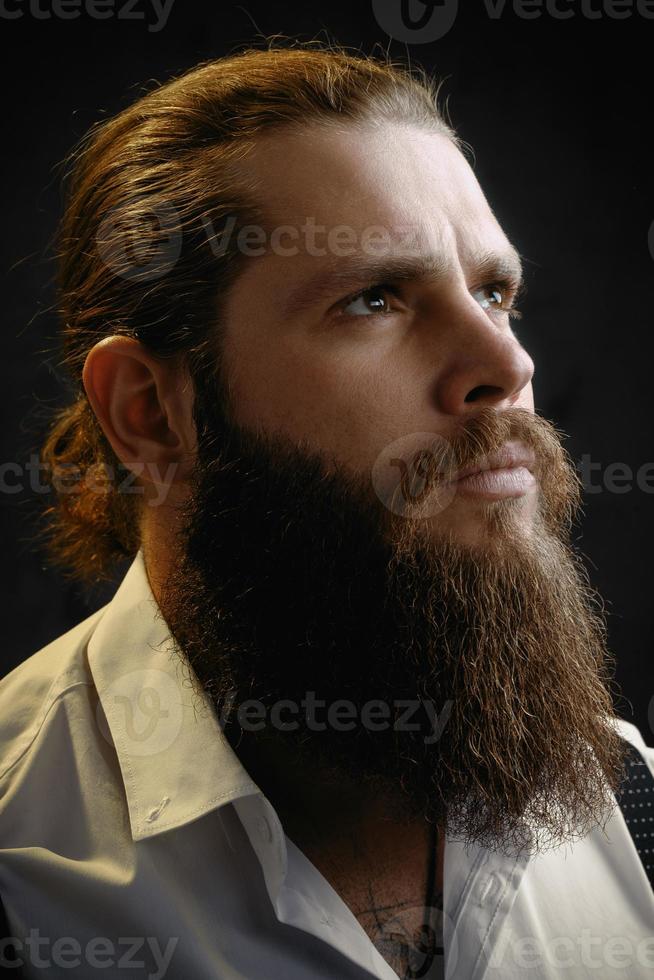 ritratto ravvicinato di un uomo brutale con barba e capelli lunghi che alza lo sguardo foto