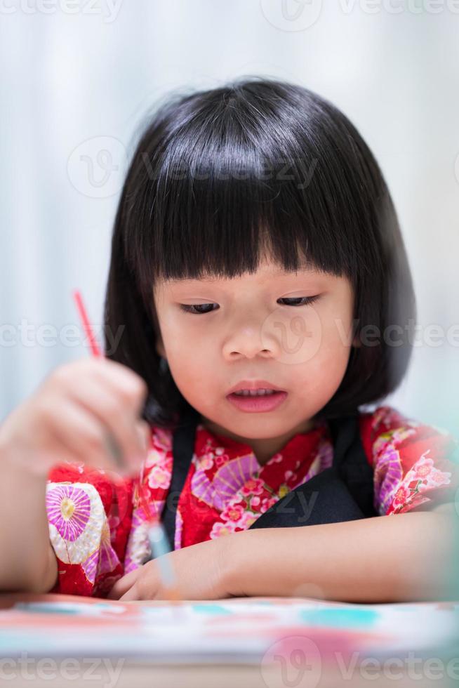 la ragazza dell'allievo si sta concentrando sul disegno e sulla pittura con pennello e acquerello su carta art. bambino asiatico indossa il grembiule mentre impara a dipingere. bambino di 3 anni. immagine verticale. foto