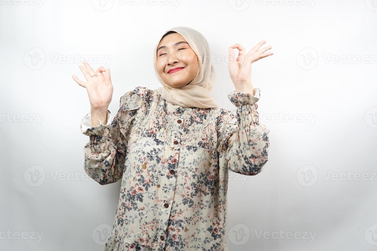 bella giovane donna musulmana con le mani che meditano segno, sorridente comodo e felice, isolato su sfondo bianco foto