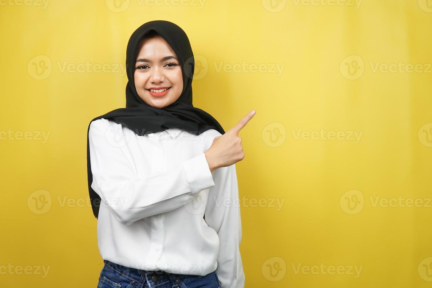 bella giovane donna musulmana asiatica con le mani che puntano lo spazio vuoto che presenta qualcosa, sorridente fiducioso, entusiasta, allegro, guardando la telecamera, isolato su sfondo giallo foto