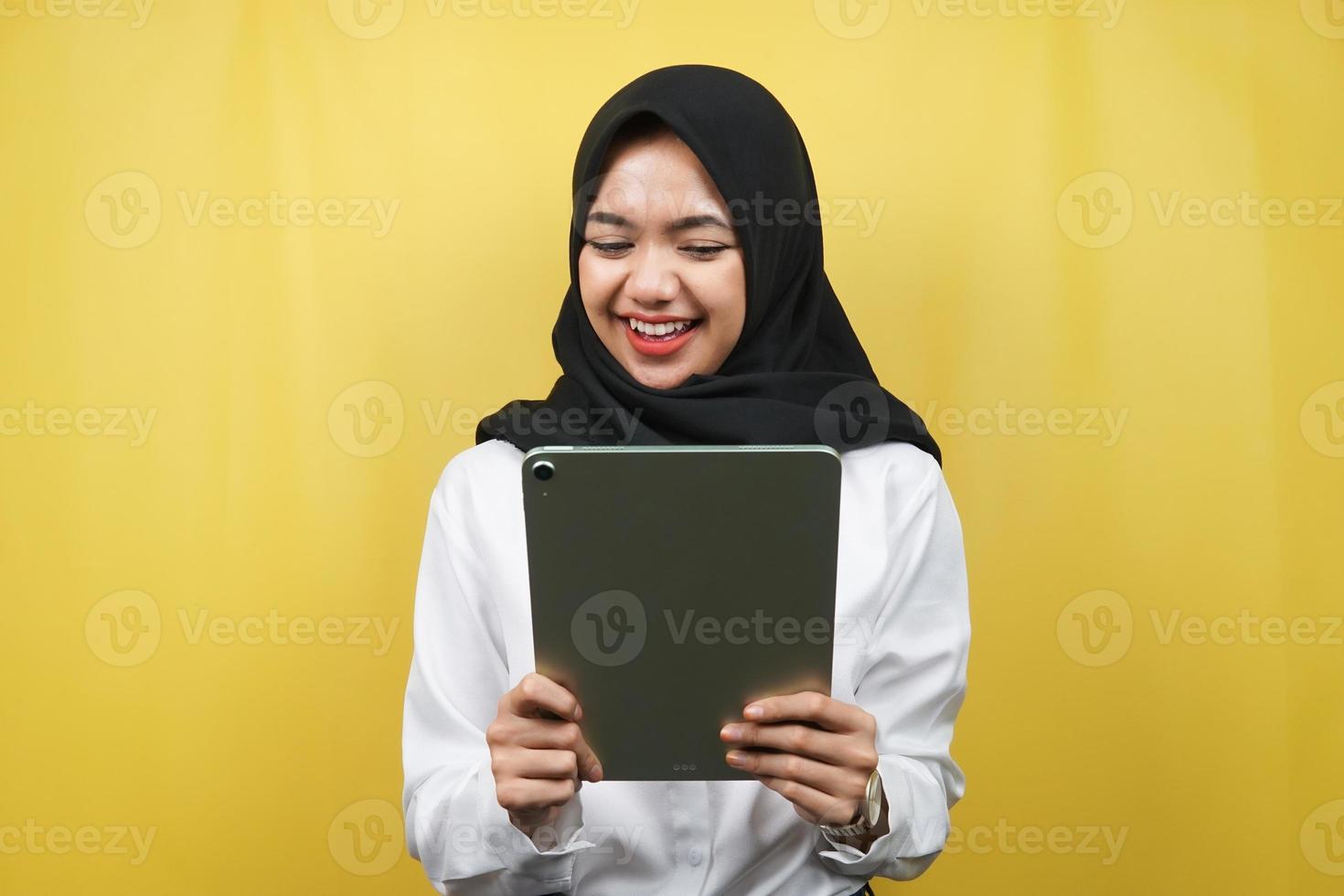 bella giovane donna musulmana asiatica sorridente, eccitata e allegra che tiene compressa, isolata su sfondo giallo foto