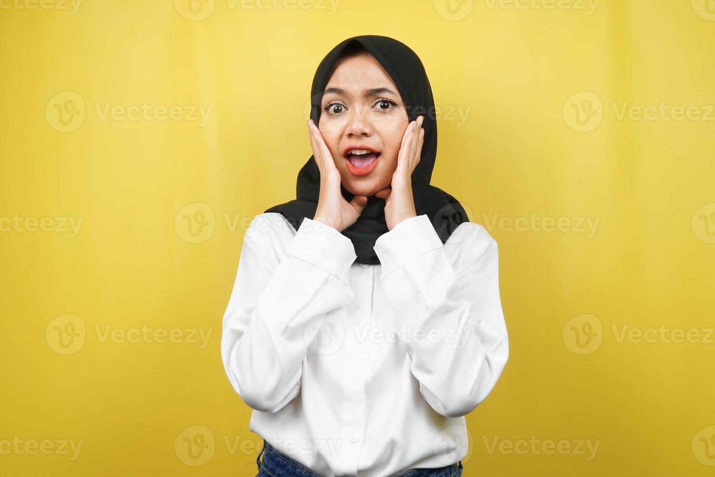 bella giovane donna musulmana asiatica scioccata, sorpresa, espressione wow, con le mani che tengono la guancia, isolata su sfondo giallo foto