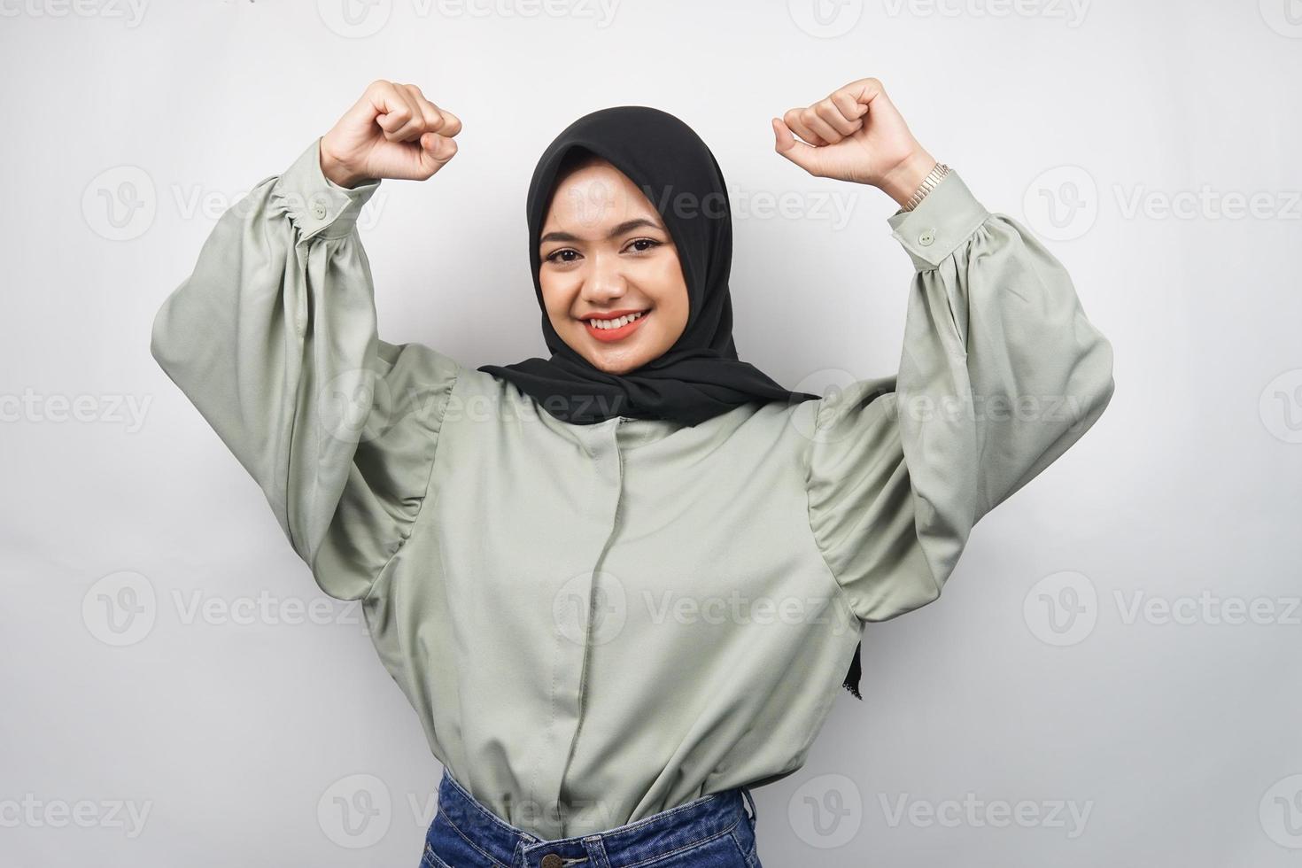 bella giovane donna musulmana asiatica sicura e sorridente, con il pugno chiuso, pugni, segno per lo spirito, combattimento, segno di vittoria, isolato su sfondo grigio foto