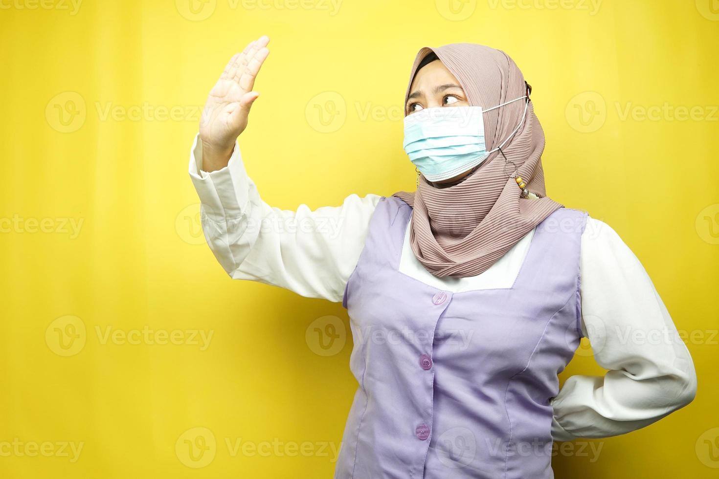 donna musulmana che indossa maschera medica con la mano che rifiuta qualcosa, mano che ferma qualcosa, mano che non gradisce qualcosa, isolato su sfondo giallo foto