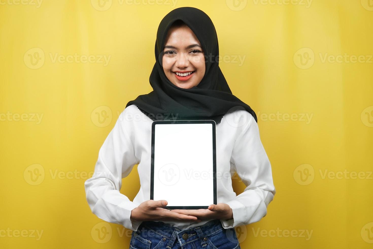 bella giovane donna musulmana asiatica sorridente, eccitata e allegra che tiene tablet con schermo bianco o vuoto, promuovendo app, promuovendo prodotto, presentando qualcosa, isolato su sfondo giallo foto