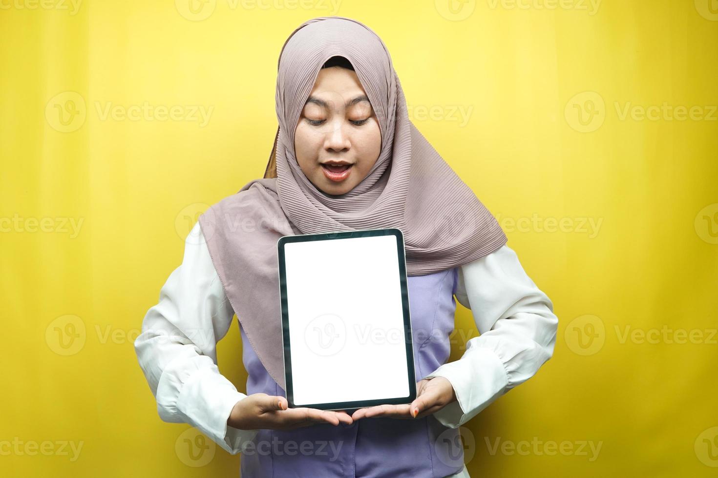 bella giovane donna musulmana asiatica sorridente, eccitata e allegra che tiene tablet con schermo bianco o vuoto, promuovendo app, promuovendo prodotto, presentando qualcosa, isolato su sfondo giallo foto