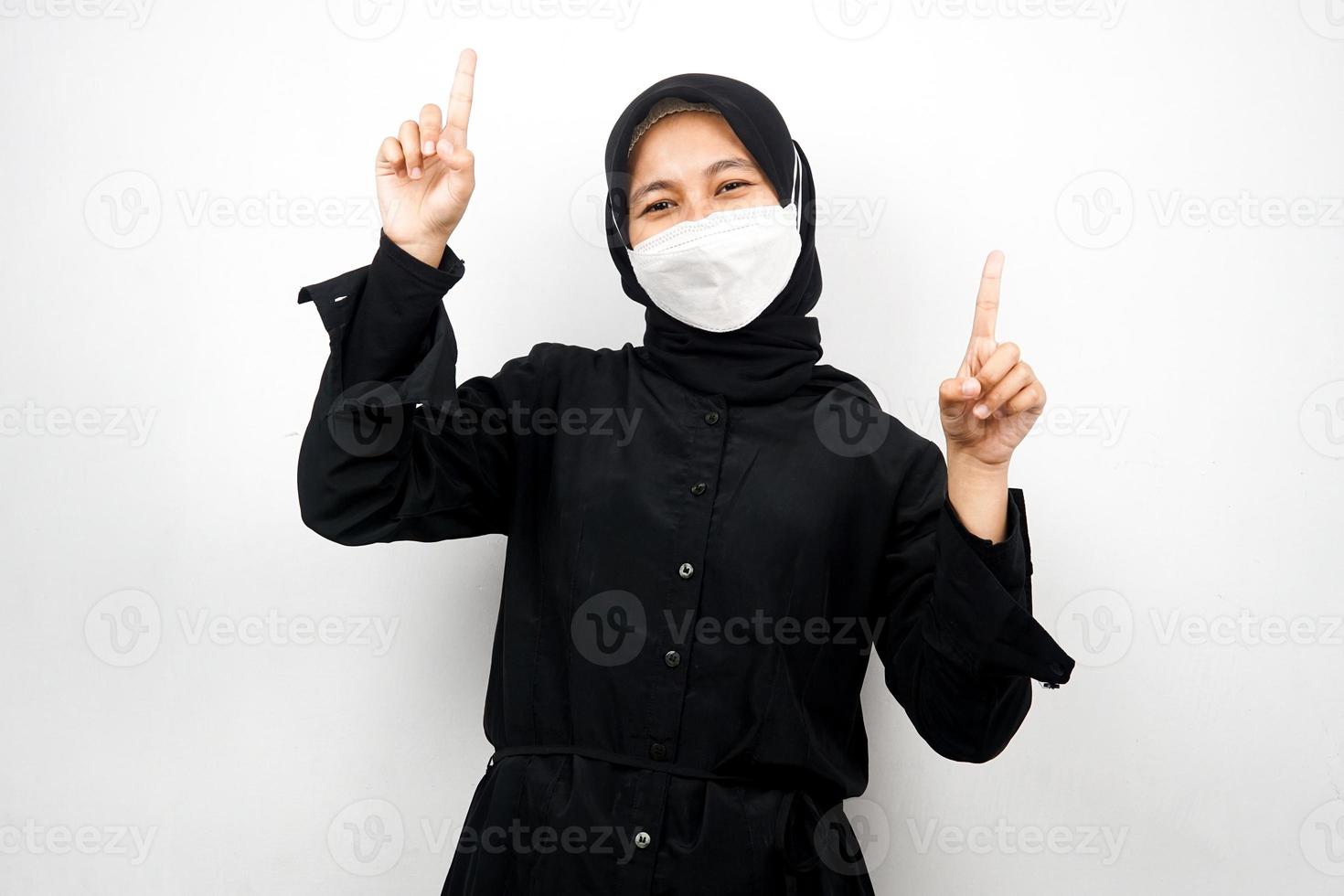 donna musulmana che indossa una maschera bianca, mano che punta allo spazio vuoto, mano che punta verso l'alto presentando qualcosa, isolato su sfondo bianco foto