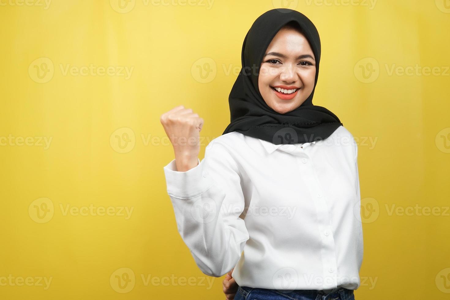 bella giovane donna musulmana asiatica sorridente sicura di sé, entusiasta e allegra con le mani serrate, segno di successo, pugni, combattimento, non paura, vittoria, isolato su sfondo giallo foto