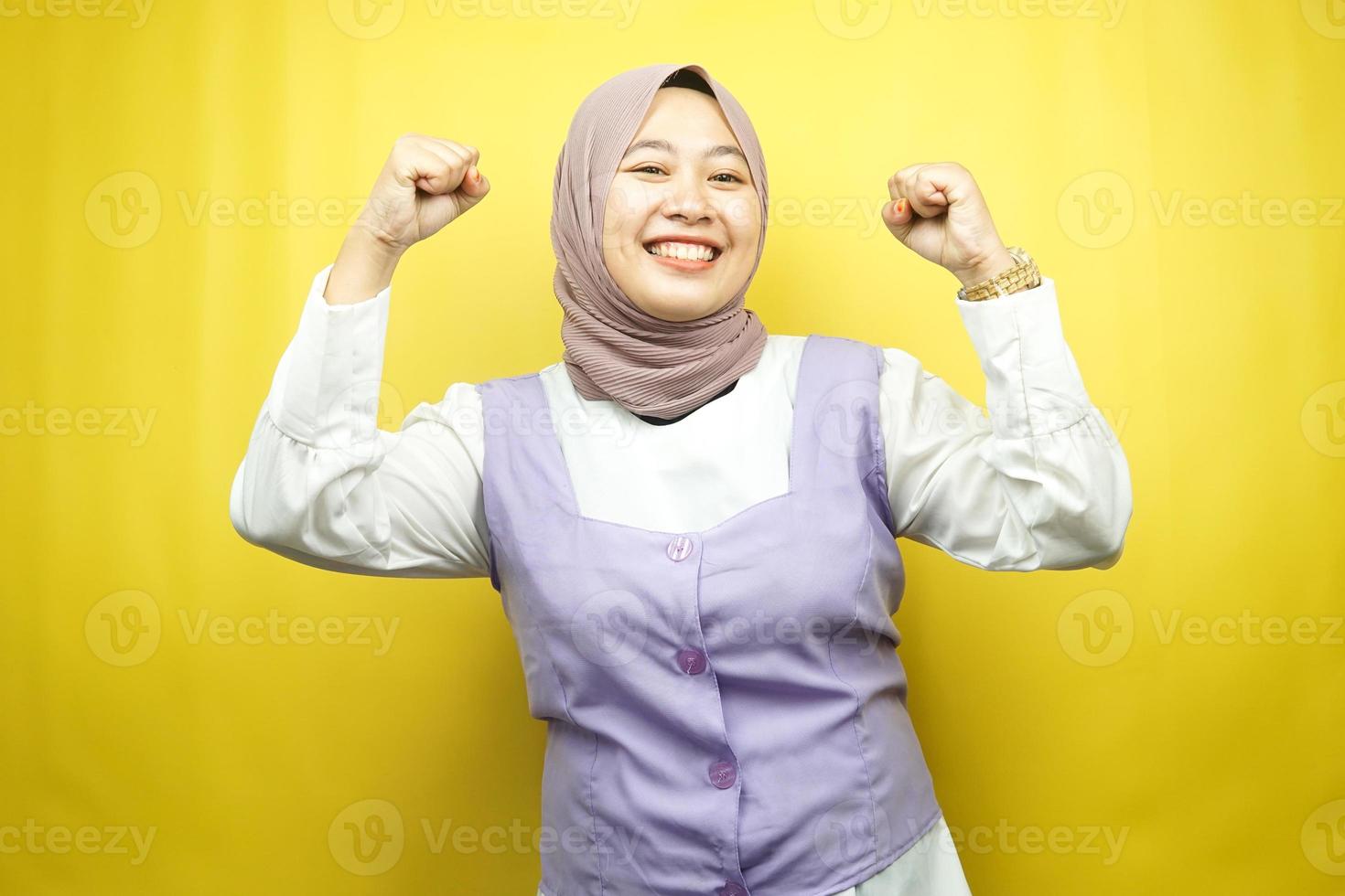 bella giovane donna musulmana asiatica sorridente sicura di sé, entusiasta e allegra con le mani serrate, segno di successo, pugni, combattimenti, non paura, isolata su sfondo giallo foto