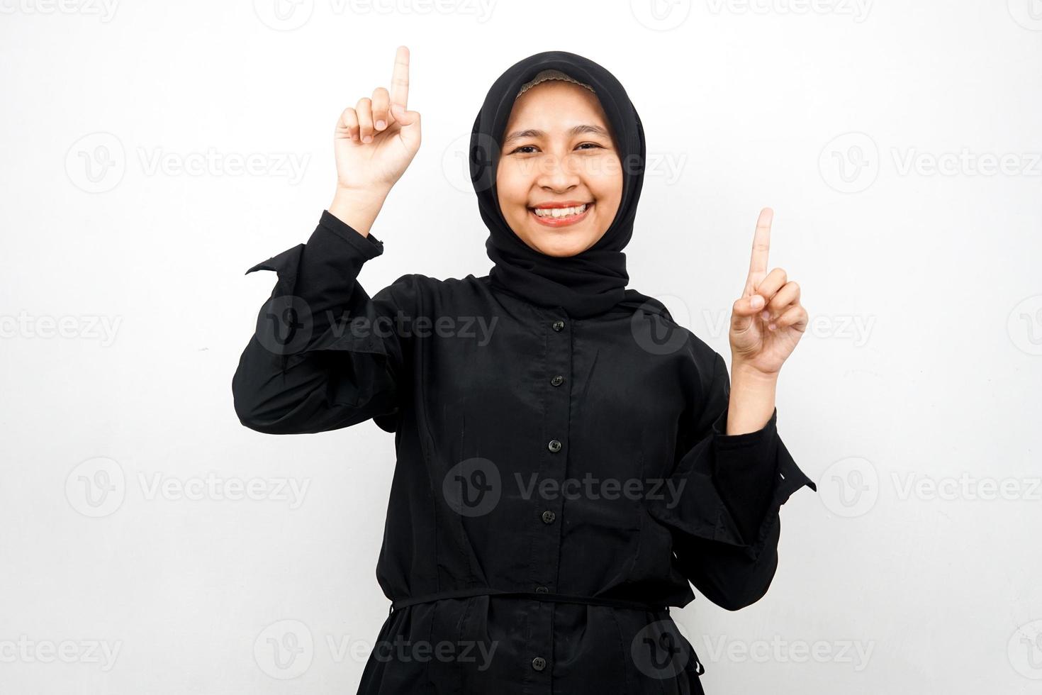 bella giovane donna musulmana asiatica sorridente sicura di sé, entusiasta e allegra con le mani rivolte verso l'alto presentando qualcosa, guardando la telecamera isolata su sfondo bianco, concetto pubblicitario foto