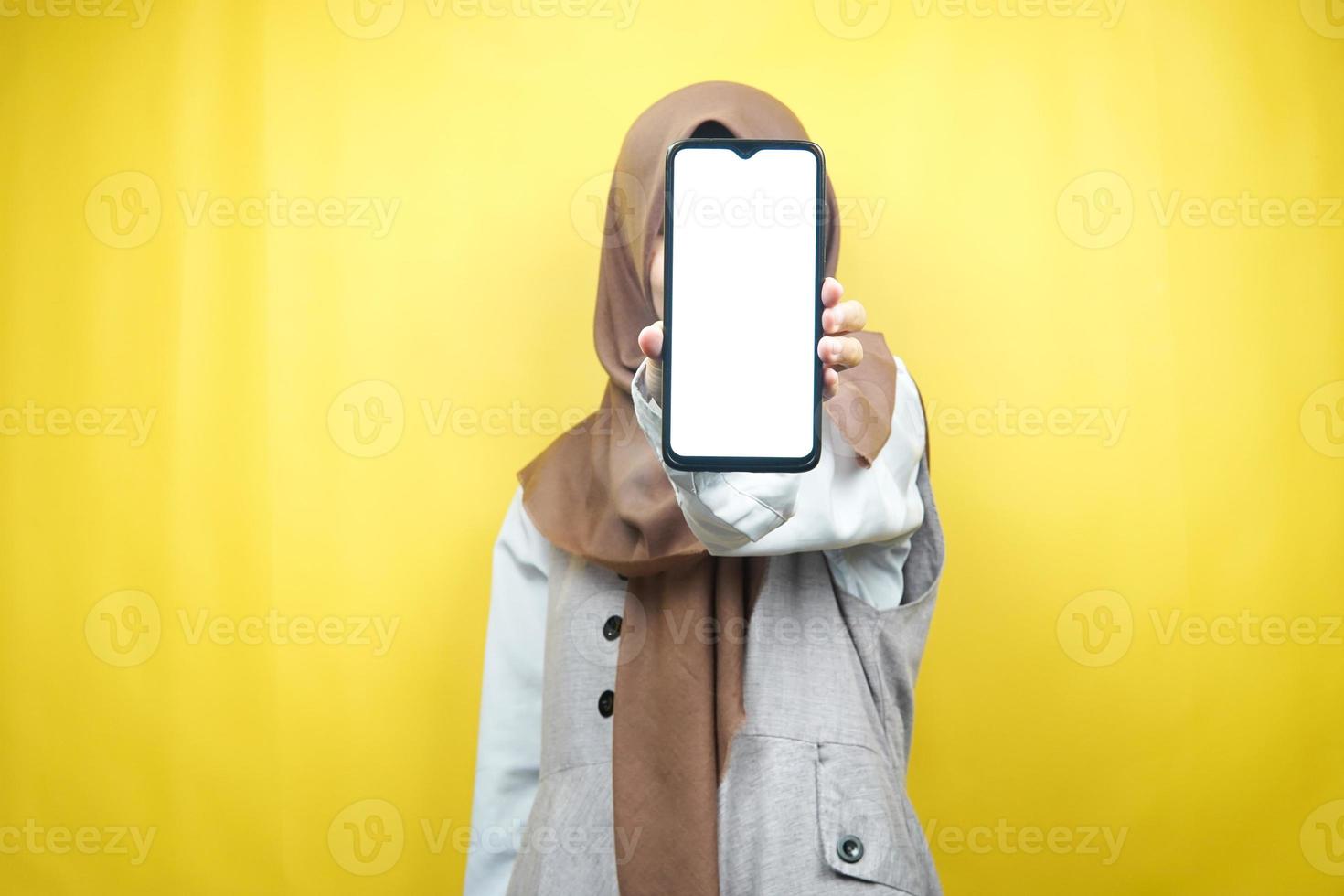 donna musulmana con le mani che tengono smartphone, promozione di app, promozione di qualcosa, isolata su sfondo giallo, concetto pubblicitario foto